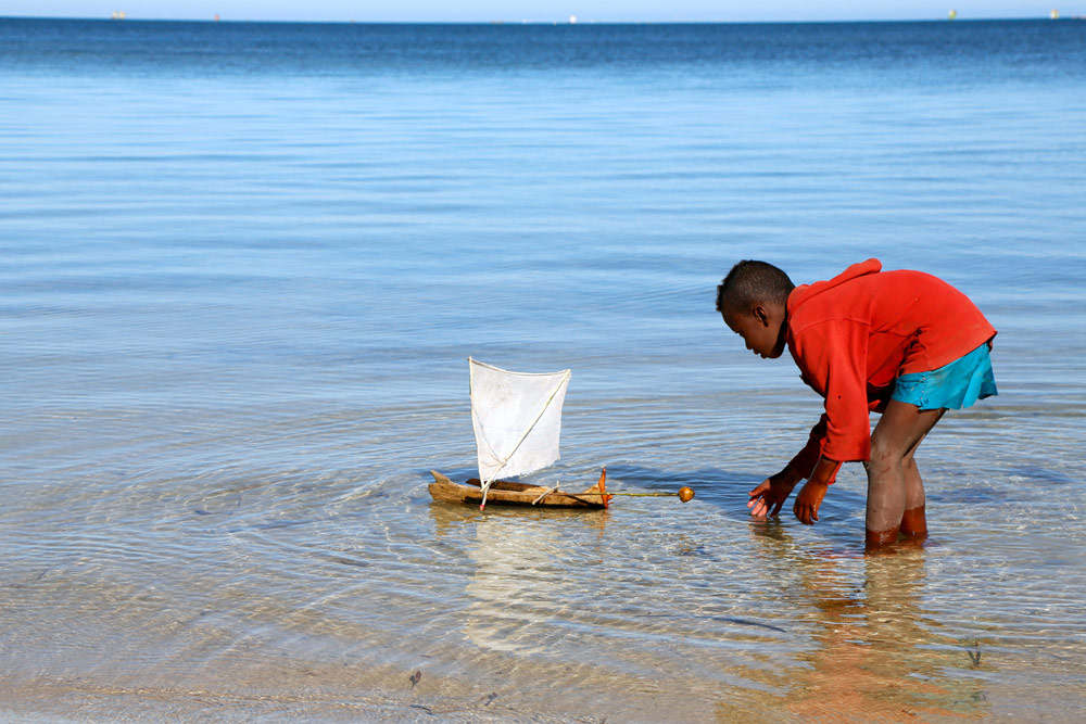 Jongen speelt met een zelfgemaaktzeil bootje Op vakantie naar Madagascar, Madagaskar, rondreis