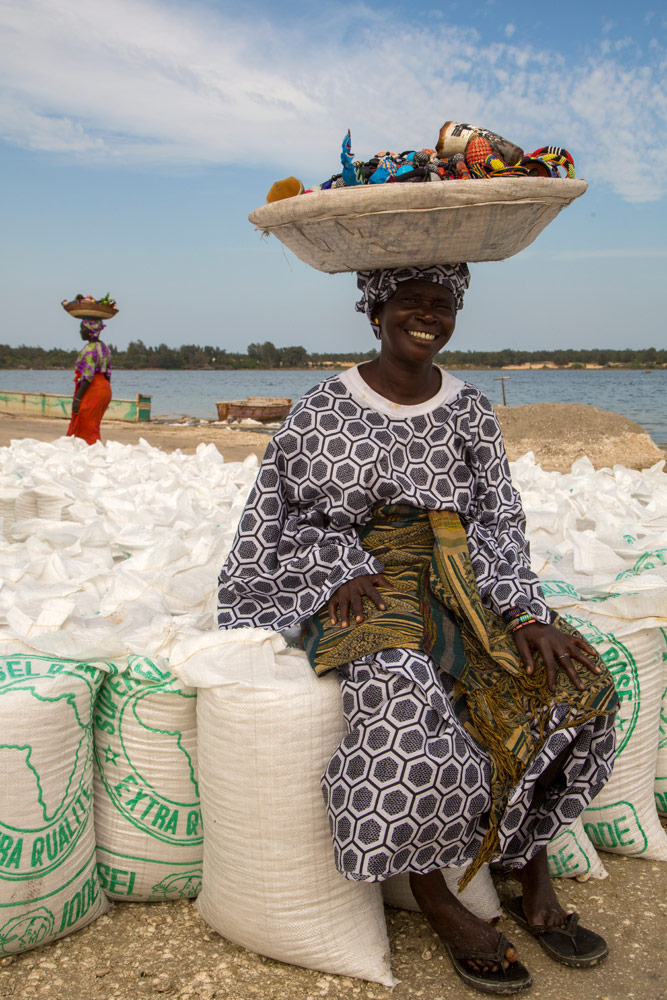 Souvenirverkoopster rust uit op zakken gevuld met zout, Lac rose, . Rondreis Senegal, Afrika, tips vakantie