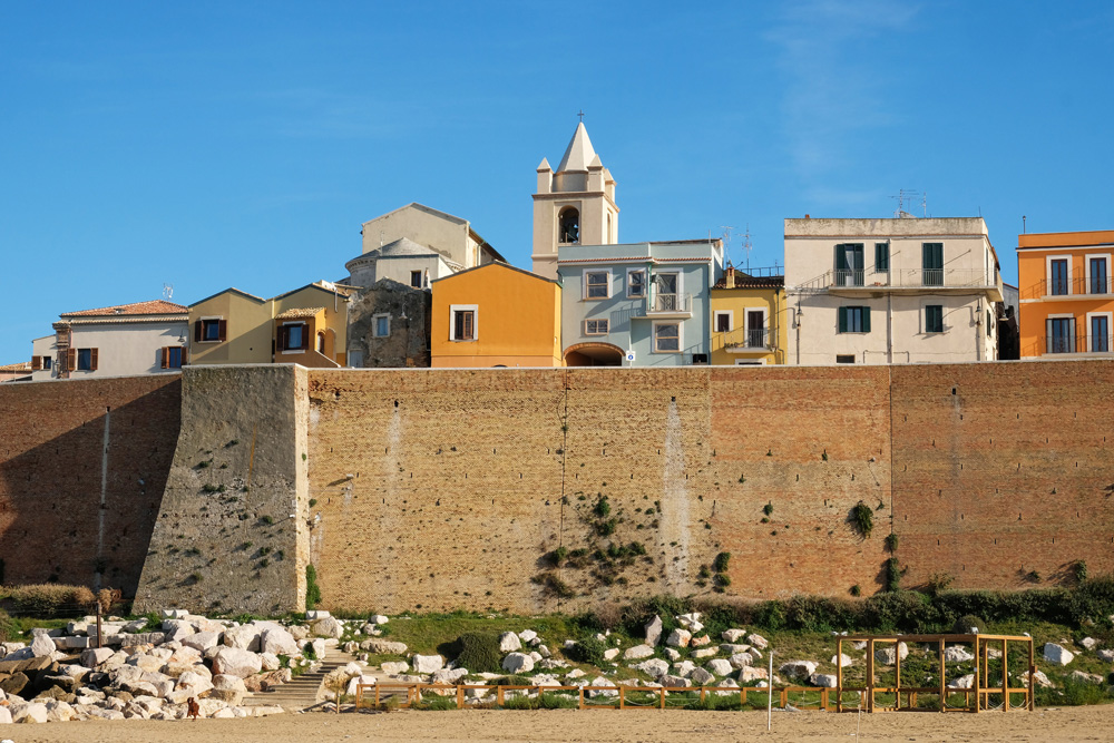 Boven de stadswal pieken de pastelkleurige huizen uit. Termoli, Molise, Zuid-Italie, rondreis, kustplaats, zomervakantie